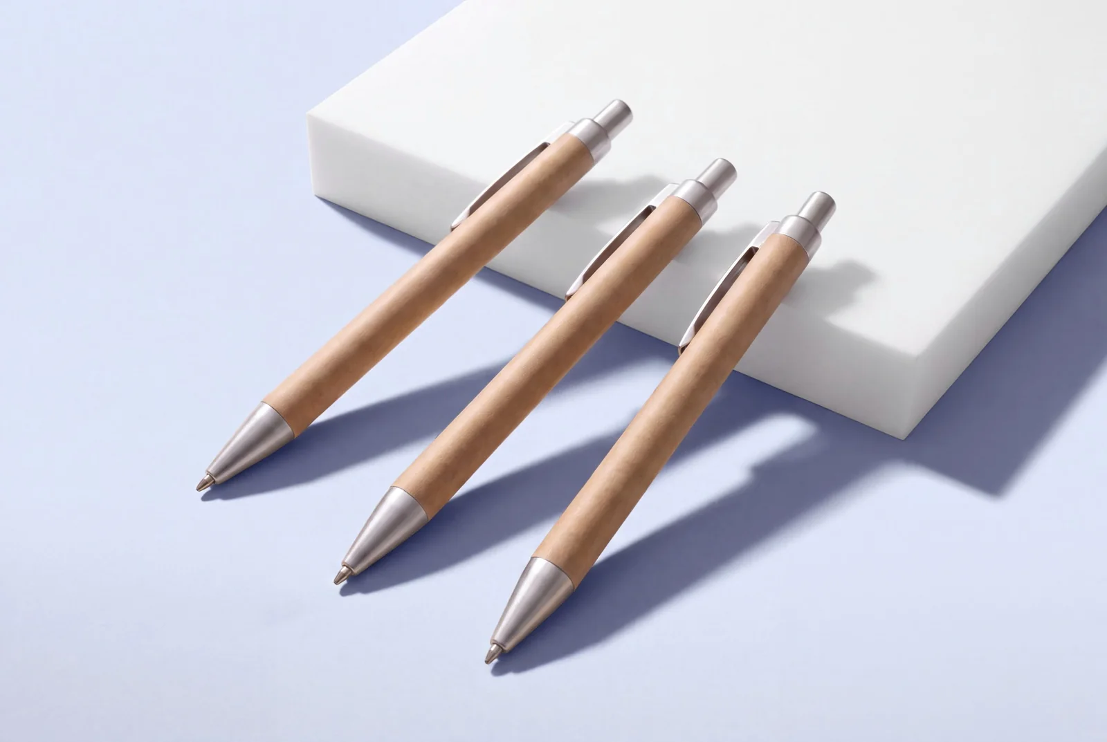 Three kraft paper ballpoint pens with silver clips and tips, resting against a white block