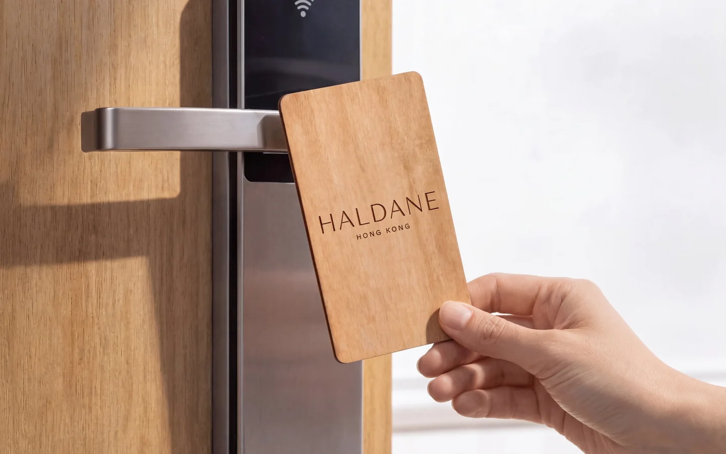 A hand holding a laser engraved wooden RFID key card for a fictional hotel up to a guest room door lock