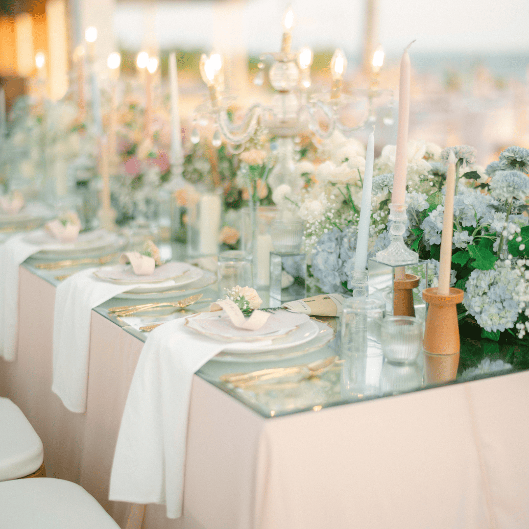Elegant wedding table setting with gold utensils, white napkins, glowing candles, and floral centerpieces.