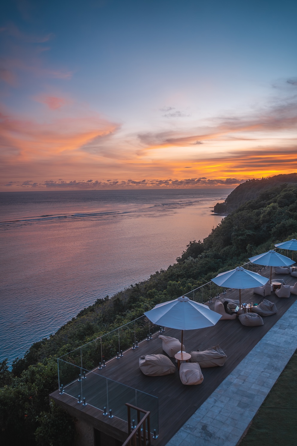 Ocean view with sunset sky above a terrace featuring umbrellas and cushioned seating.