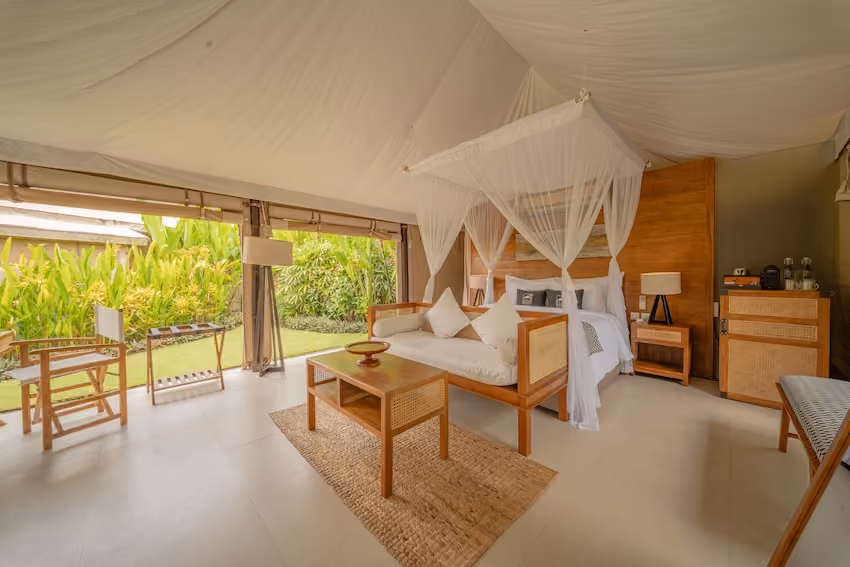Bright tented bedroom with wooden furniture, a canopy bed, and an open view to lush greenery outside.