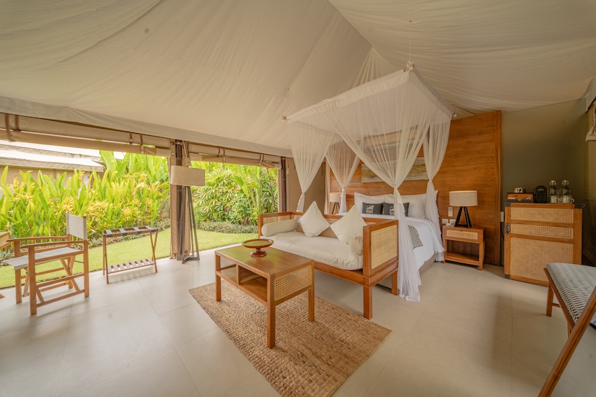 Bright tented bedroom with wooden furniture, a canopy bed, and an open view to lush greenery outside.