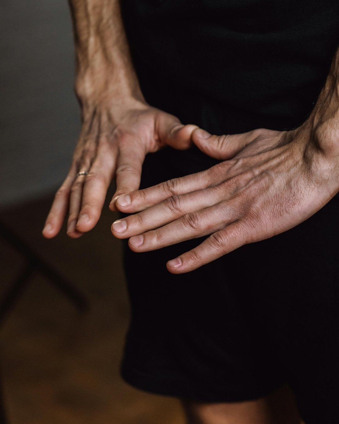 Close-up of two adult hands with visible veins against a dark background.