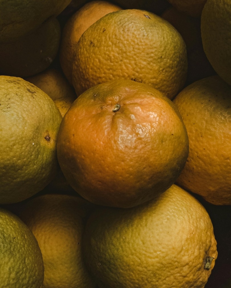 Close-up of a pile of ripe oranges with textured skin and natural blemishes.