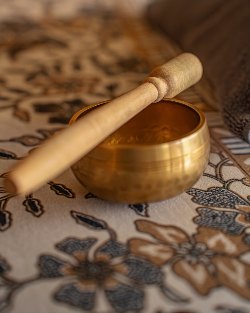 Brass singing bowl with wooden mallet resting on a patterned fabric surface.