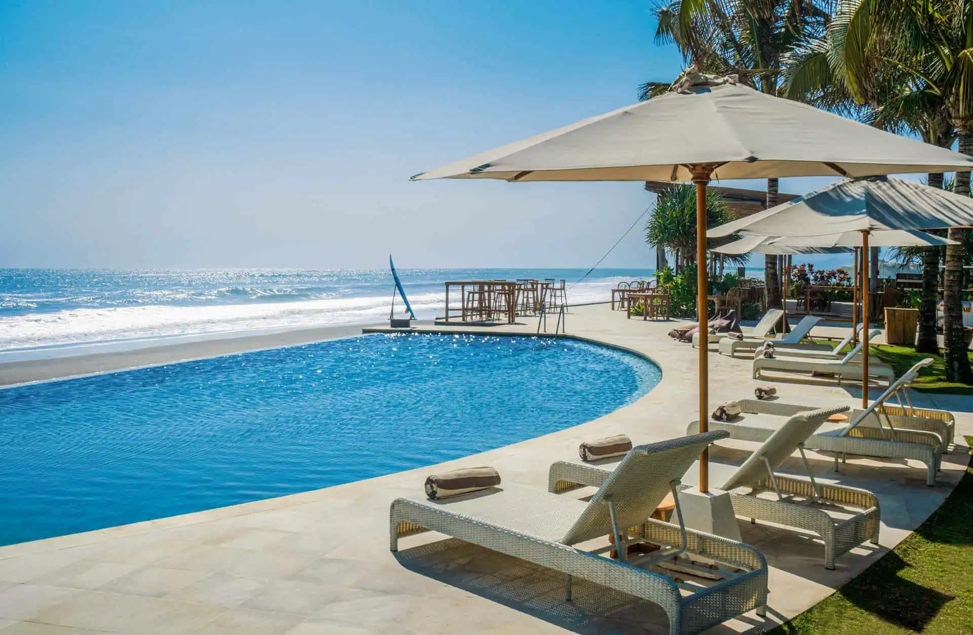 Infinity pool overlooking ocean beach with lounge chairs and umbrellas on the pool deck.