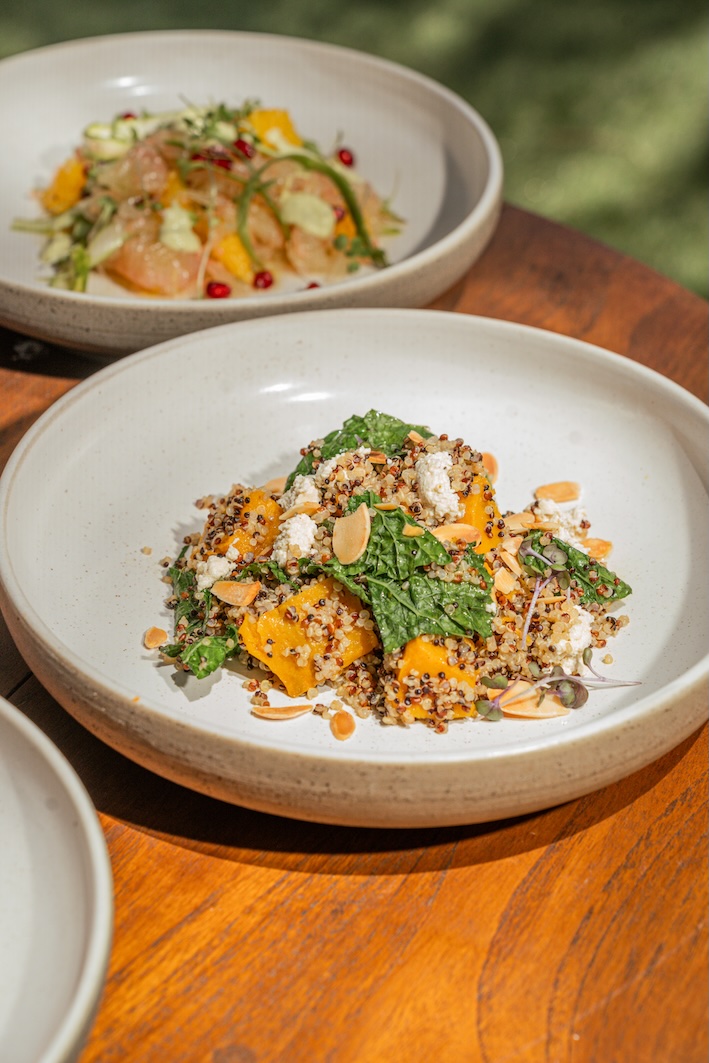 Plate of quinoa salad with kale, roasted squash, goat cheese, and almond slices on a wooden table.