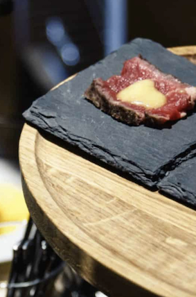 Piece of raw beef topped with a dollop of sauce served on a black slate plate on a wooden table.