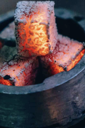Glowing red hot charcoal briquettes arranged in a metal container for shisha or grilling.