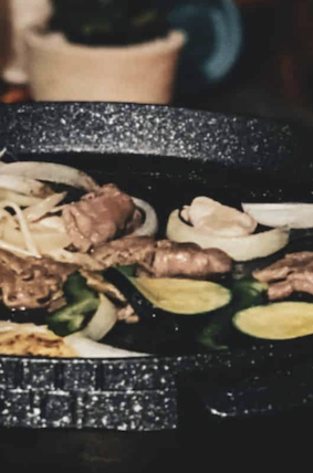 Grill pan cooking sliced meat, onions, zucchini, and green peppers.