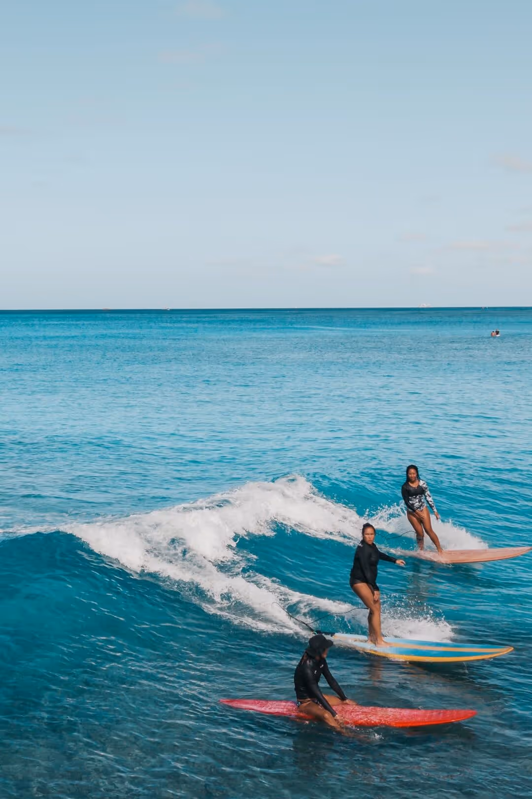 Three surfers riding and sitting on surfboards in clear blue ocean water under a bright sky.