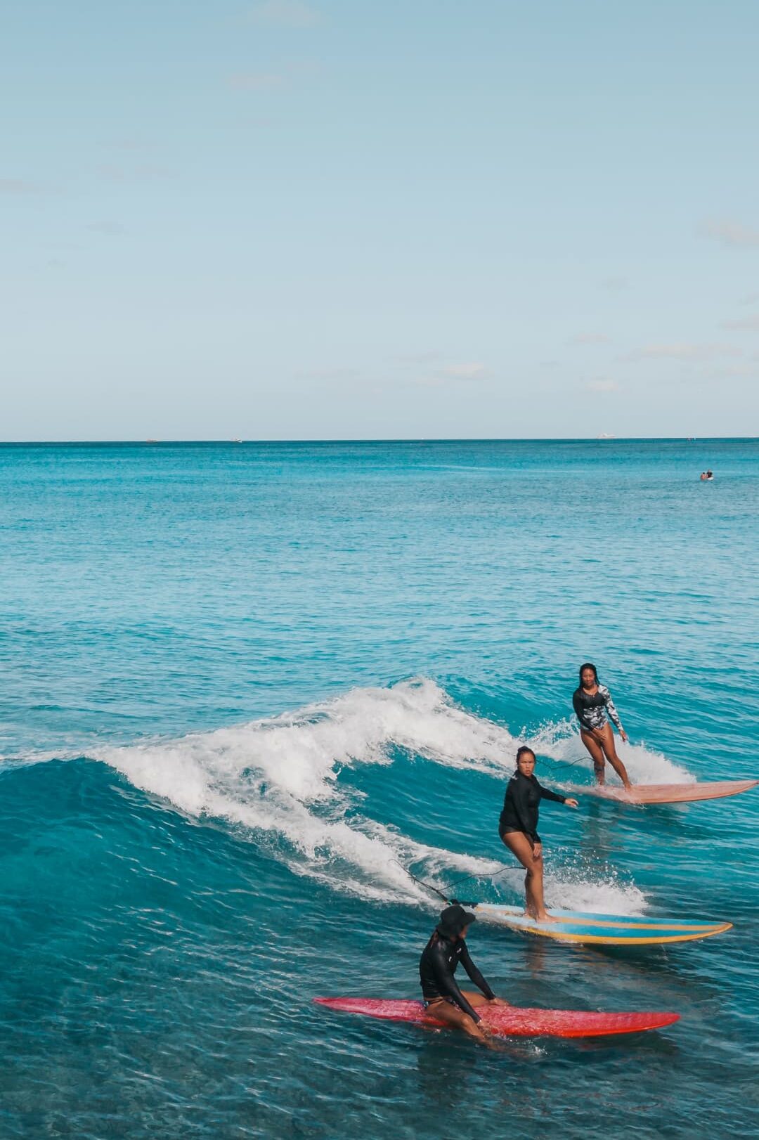 Three surfers riding and sitting on surfboards in clear blue ocean water under a bright sky.