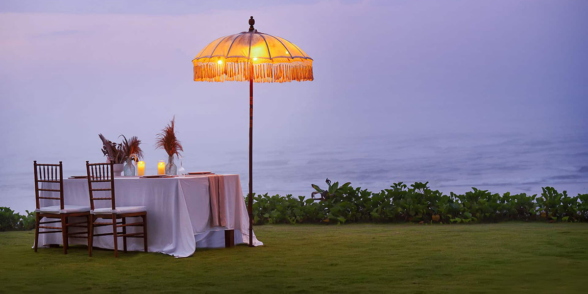 Romantic outdoor dinner setup with two chairs, a table with candles, and a glowing umbrella near water.
