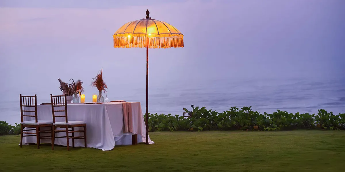 Romantic outdoor dinner setup with two chairs, a table with candles, and a glowing umbrella near water.