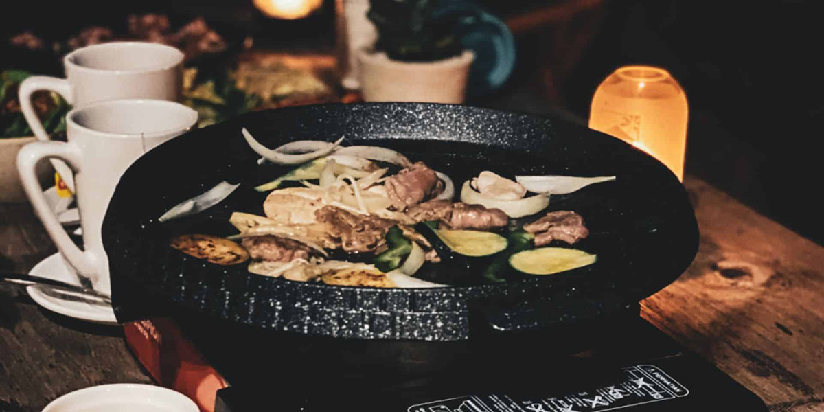 Korean BBQ grilling meat, onions, and zucchini slices on a tabletop pan with dim lighting.