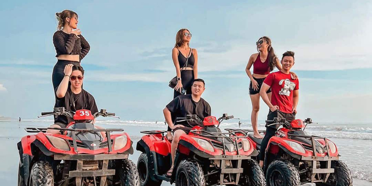 Group of six young people posing on three red ATVs on a beach under a blue sky.