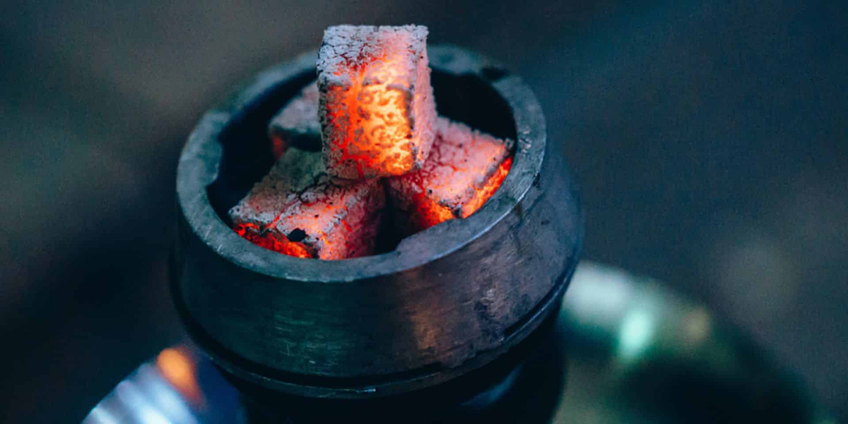 Close-up of glowing hot coals in a round metal container, used for heating shisha or hookah.