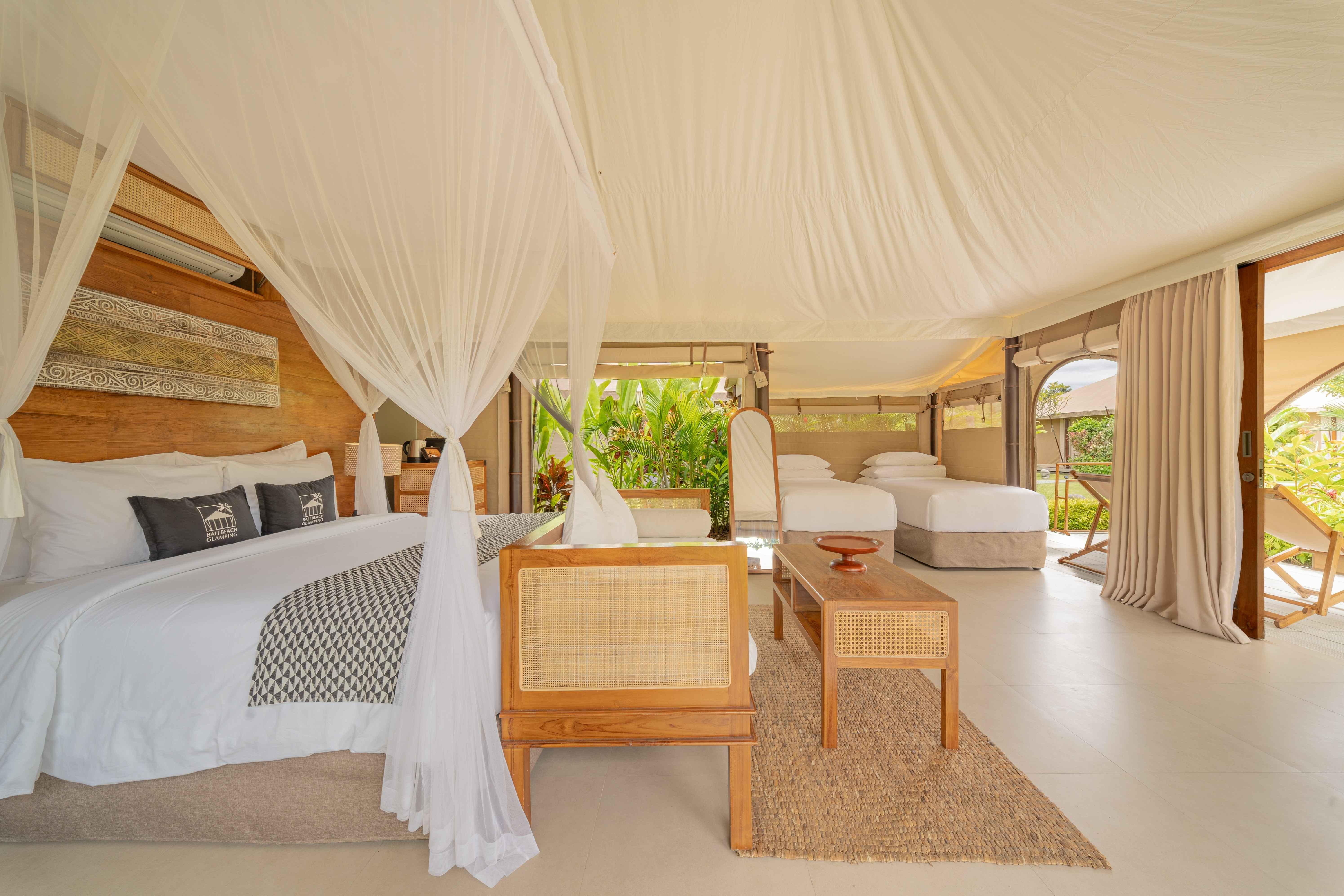 Spacious tented room with a canopy bed, two single beds, wooden furniture, and greenery outside.