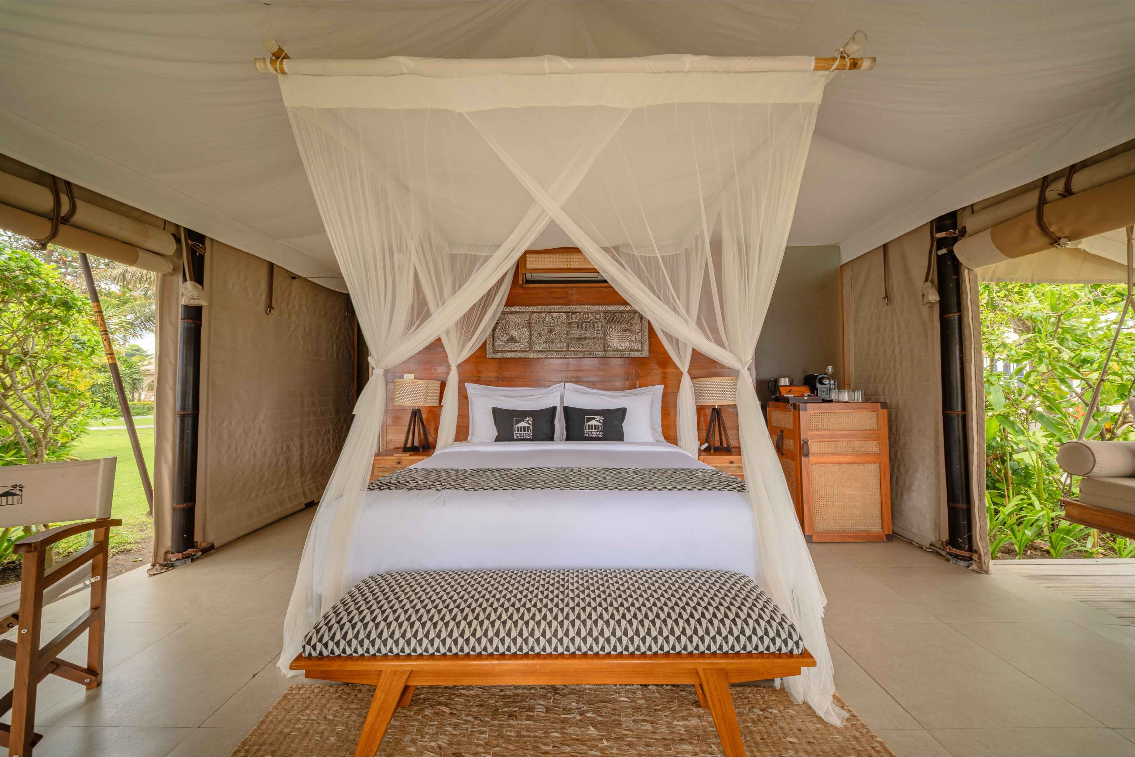 Elegant bedroom with a canopy bed draped in sheer curtains, wooden bench, and leafy outdoor views.