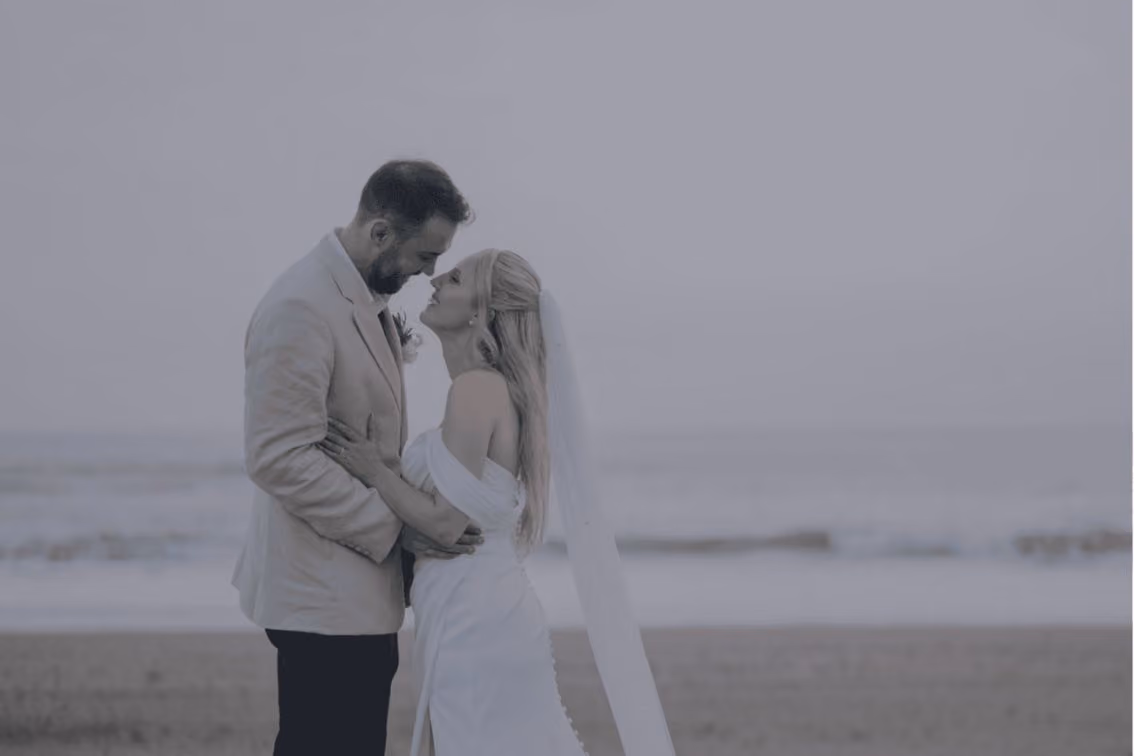 Bride and groom embracing and gazing into each other's eyes on a beach at sunset.