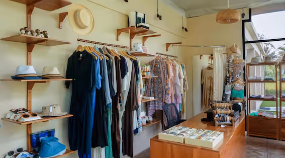 Boutique interior with wooden shelves displaying dresses, hats, bags, and jewelry in a well-lit room.