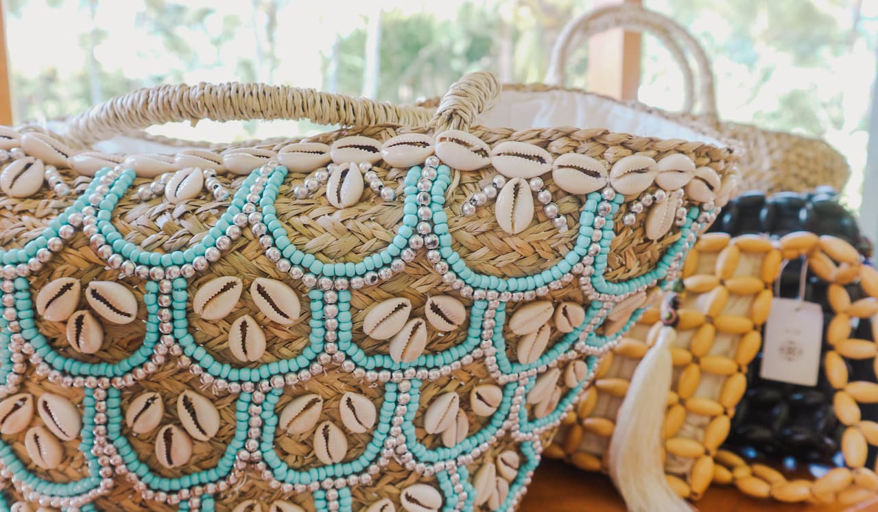 Handwoven straw bags decorated with seashells, turquoise beads, and silver accents on a wooden surface.