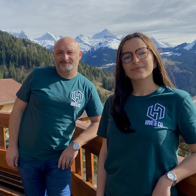 Deux membres de l’équipe Hive en t-shirts de marque devant un panorama de montagne enneigée