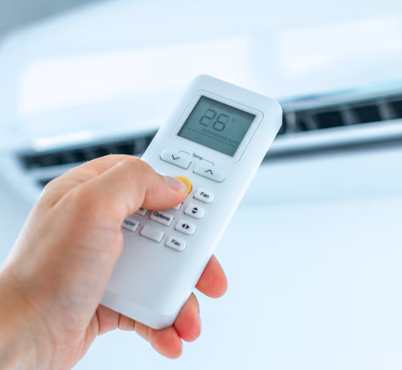 Main tenant une télécommande climatisation affichant 26°C devant unités intérieures