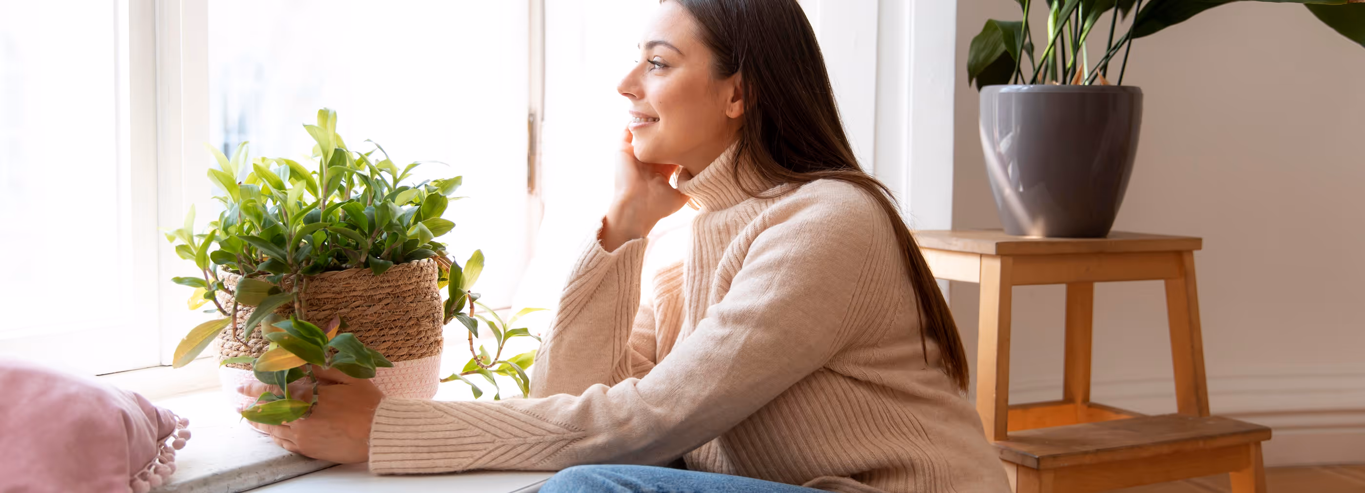 Femme souriante regardant par la fenêtre, entourée de plantes vertes en pots