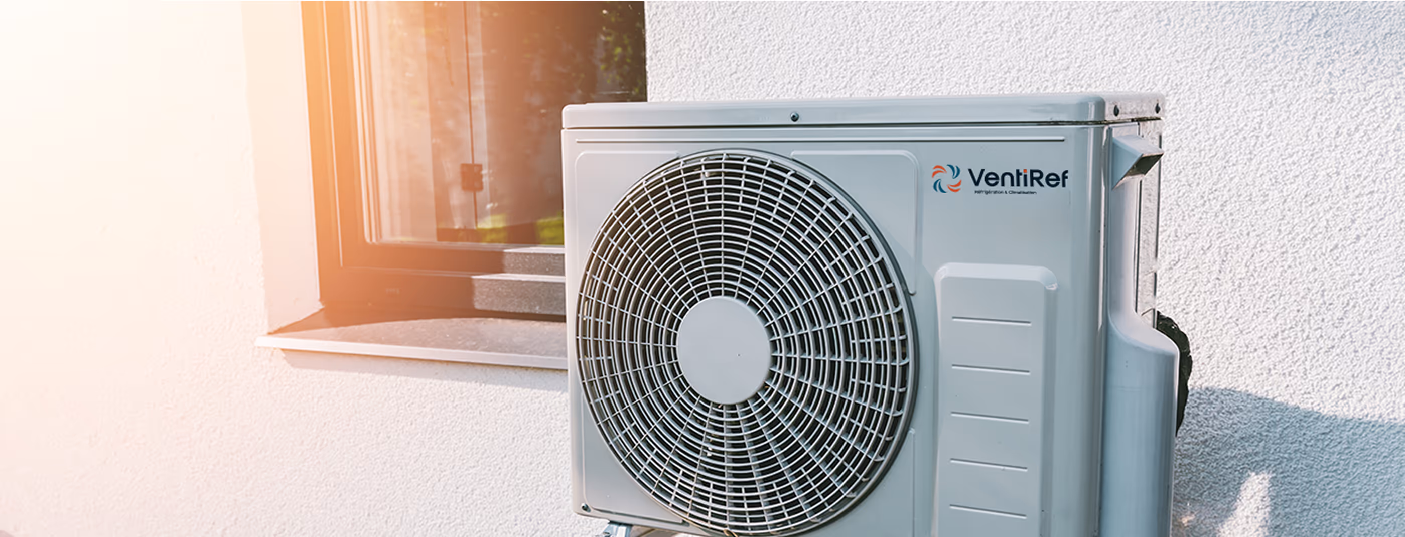 Unité extérieure de climatisation VentiRef grise fixée au mur blanc d'une maison.