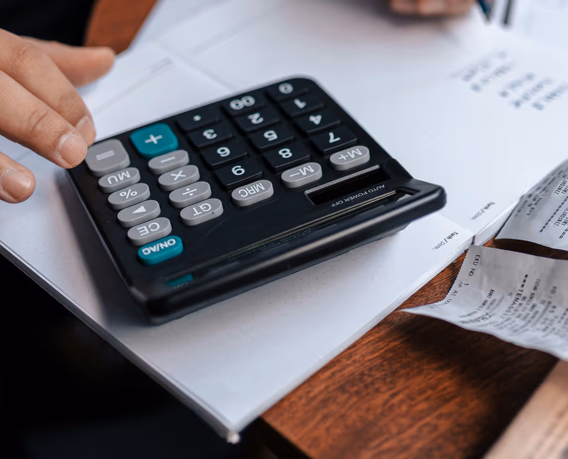 Une personne utilise une calculatrice noire sur des documents financiers et des factures papier.