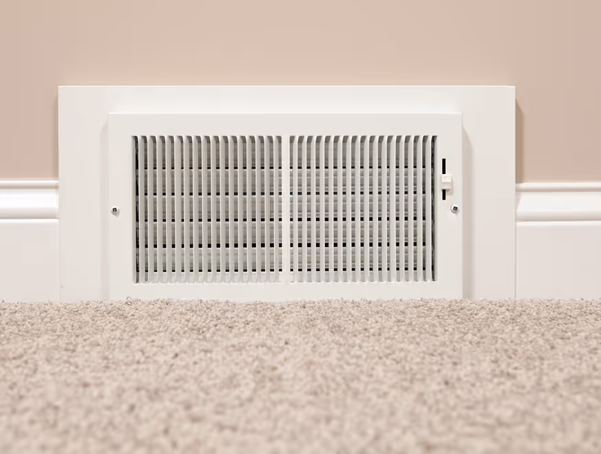 Grille de ventilation blanche rectangulaire encastrée dans le mur avec tapis beige au sol