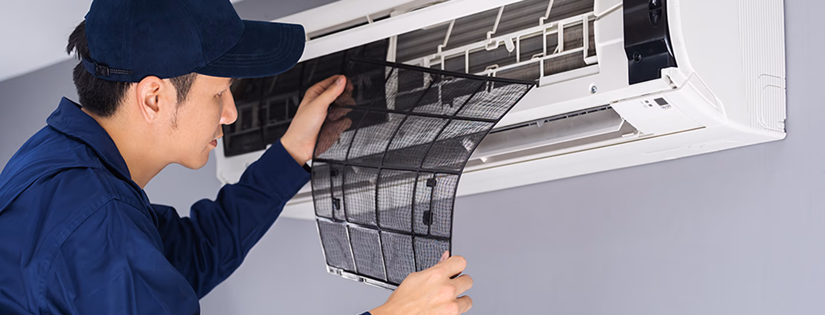 Technicien en uniforme bleu nettoyant le filtre d'un climatiseur mural blanc