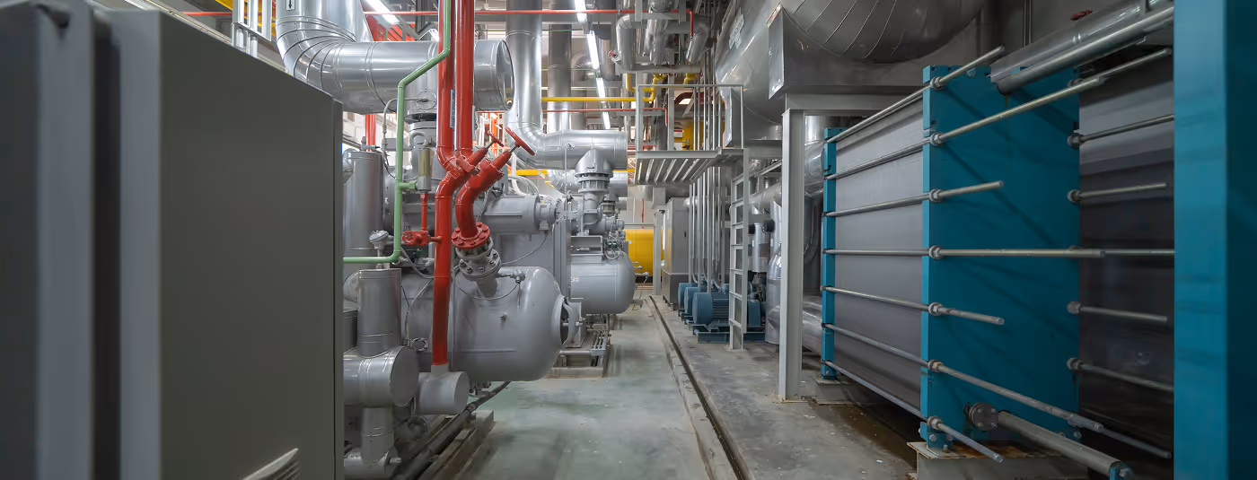 Couloir industriel avec tuyauterie rouge et grise, équipements mécaniques complexes.