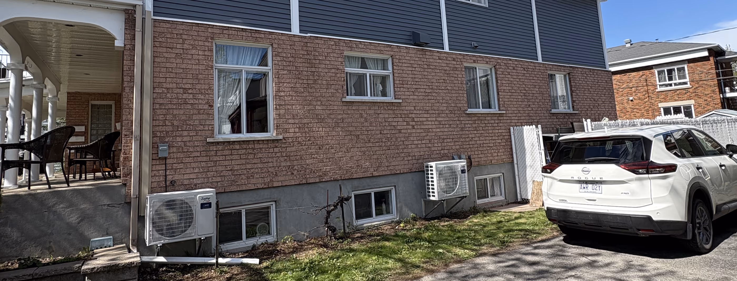 Maison en brique rouge avec voiture blanche garée dans l'allée et climatiseurs