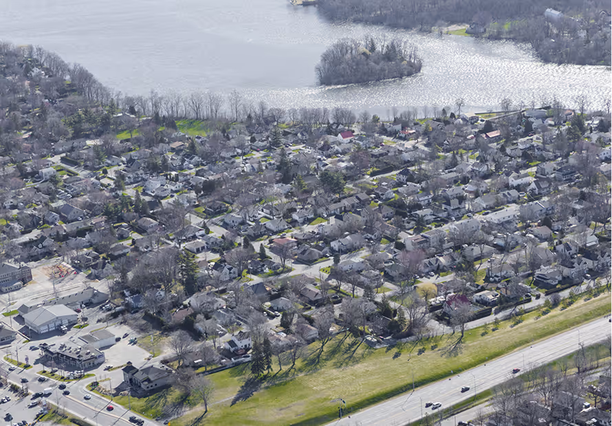 Vue aérienne d'une banlieue avec maisons, route et rivière en arrière-plan.