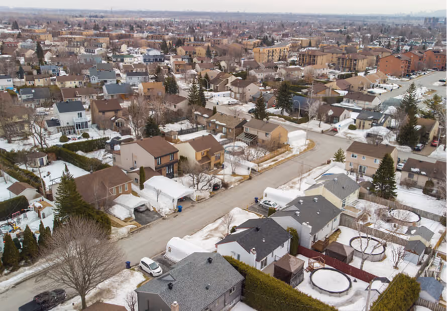 Vue aérienne d'un quartier résidentiel avec maisons, neige et arbres épars.