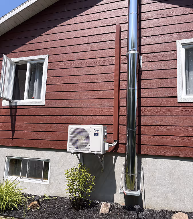 Façade de maison rouge avec climatiseur, tuyau métallique et petits arbustes verts