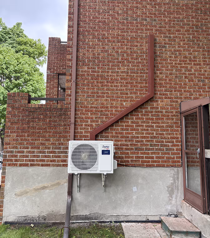 Climatiseur blanc fixé à un mur de brique rouge avec escaliers métalliques.