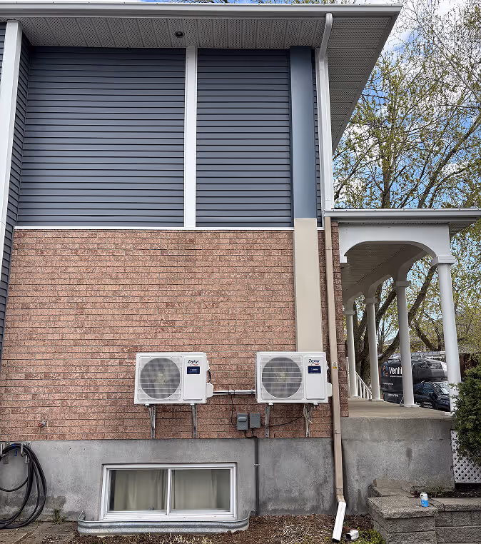 Maison moderne avec volets gris, briques rouges et deux climatiseurs muraux externes