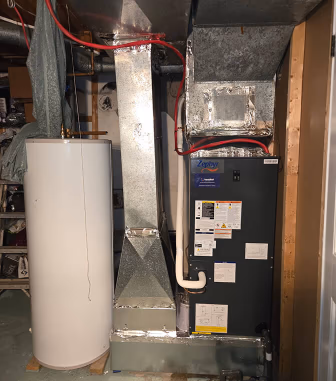 Chaudière électrique noire et réservoir blanc cylindrique dans un sous-sol.