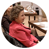 Woman with curly hair wearing a red blazer seated at a table in a meeting.