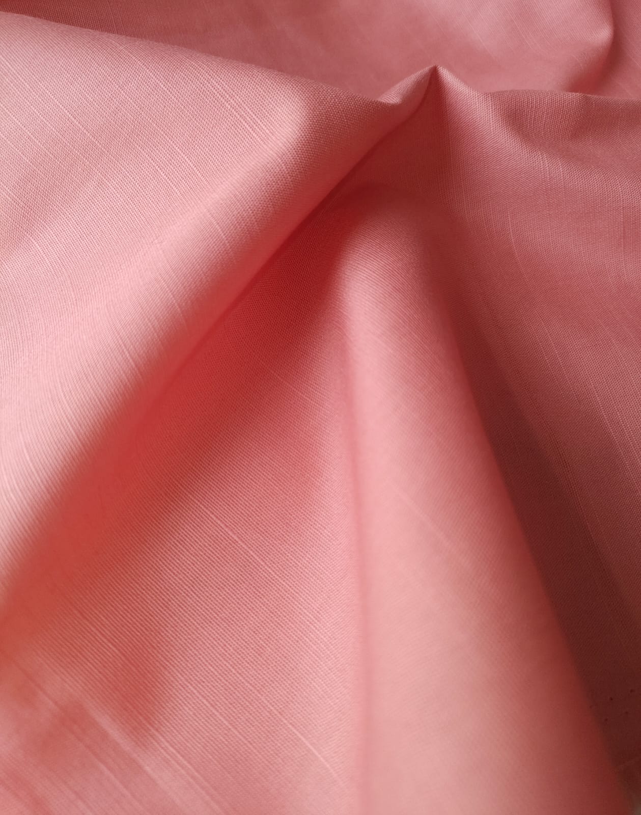 Close-up of soft, wrinkled pink cotton fabric displaying fine weave texture.