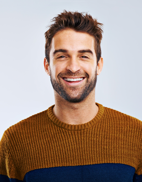 Smiling man with short brown hair and beard wearing a brown and navy blue sweater against a light background.