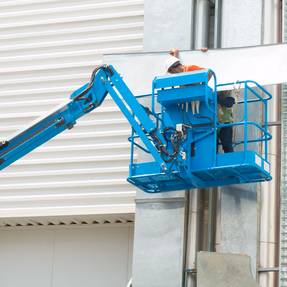 Bauarbeiter in weißem Helm auf blauer Hebebühne montiert Metallplatte an Gebäudefassade.