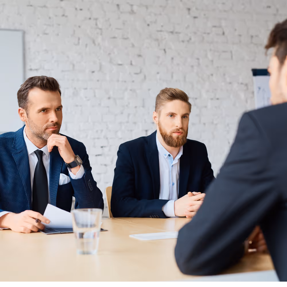 Zwei Männer in Anzügen bei einem Beratungsgespräch sitzen konzentriert dem Gesprächspartner gegenüber.