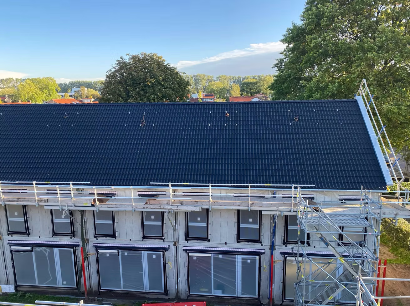 Woning in aanbouw met zwart dak en steigers rondom, rode bouwsteiger aan de rechterkant.