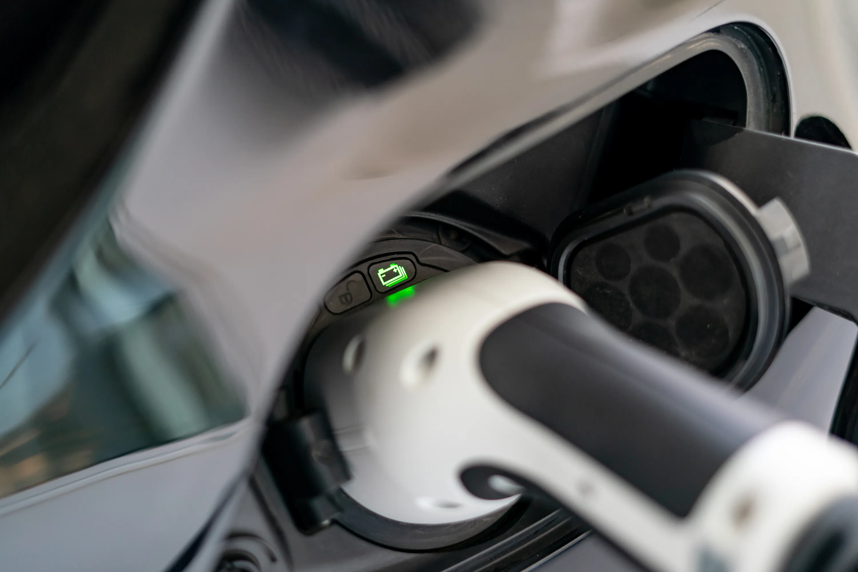 Lähikuva sähköauton latausliittimestä, jossa näkyy vihreä latausvalo ja valkoinen latausjohto.