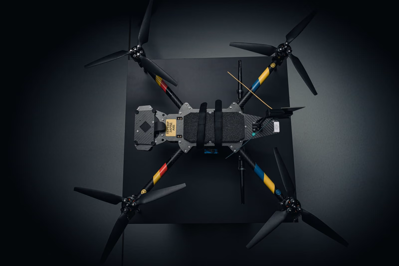 Top view of a quadcopter drone from Quantum Frontline Industries with black propellers and colorful arm stripes on a dark background.