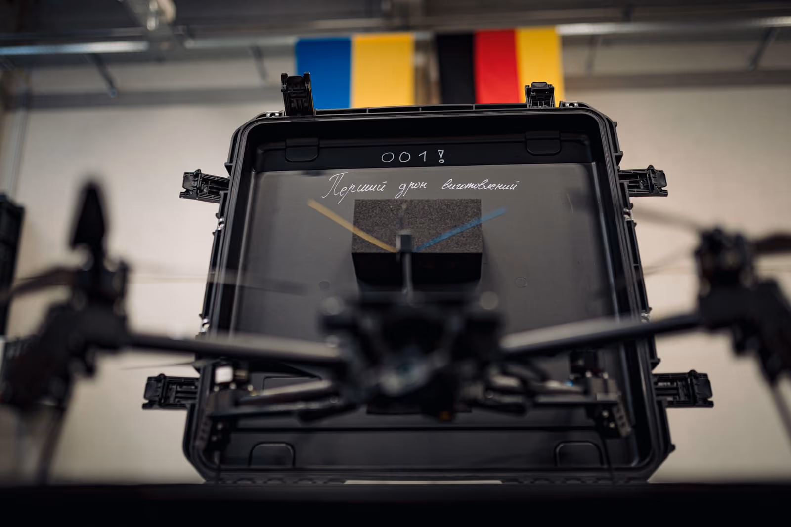 Black drone above an open hard case with colored rods and a flag with Ukrainian and German flag in background.